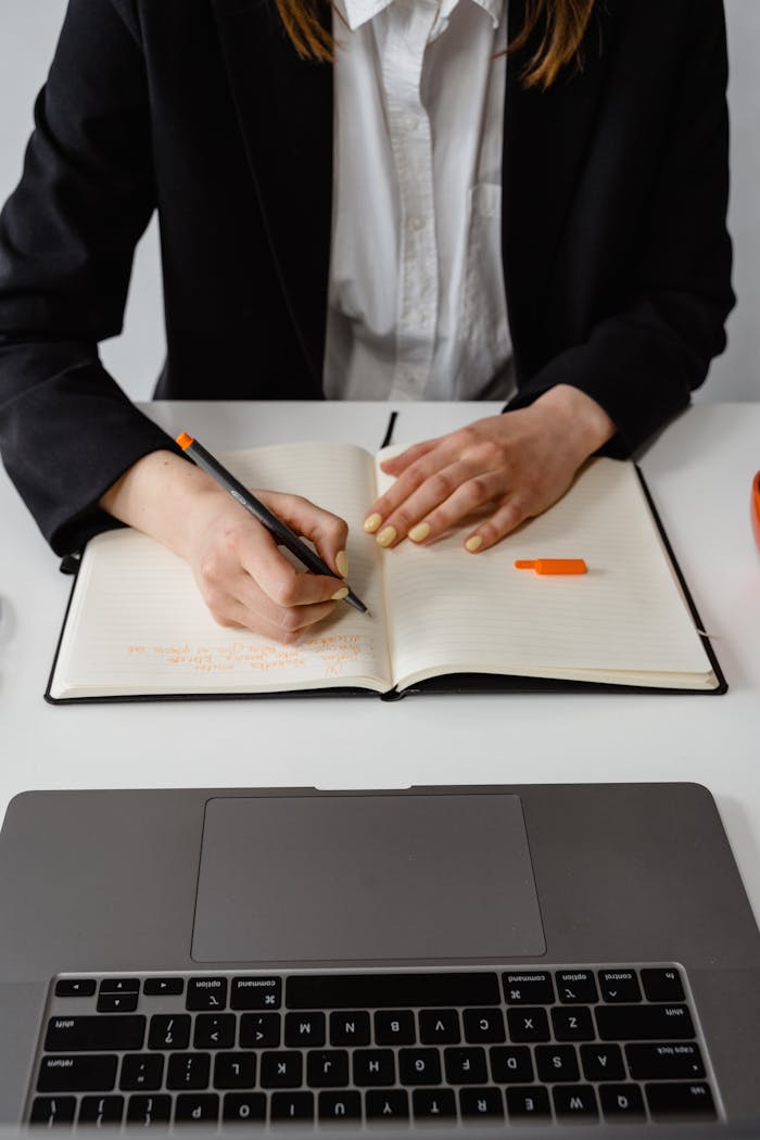 Businesswoman with notebook and laptop taking notes at a desk.